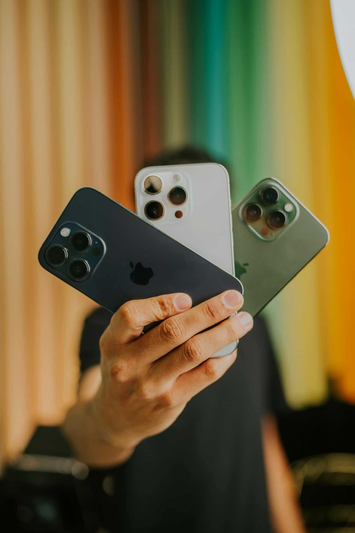 A person holding three smartphones with a colorful striped background. Modern technology concept.