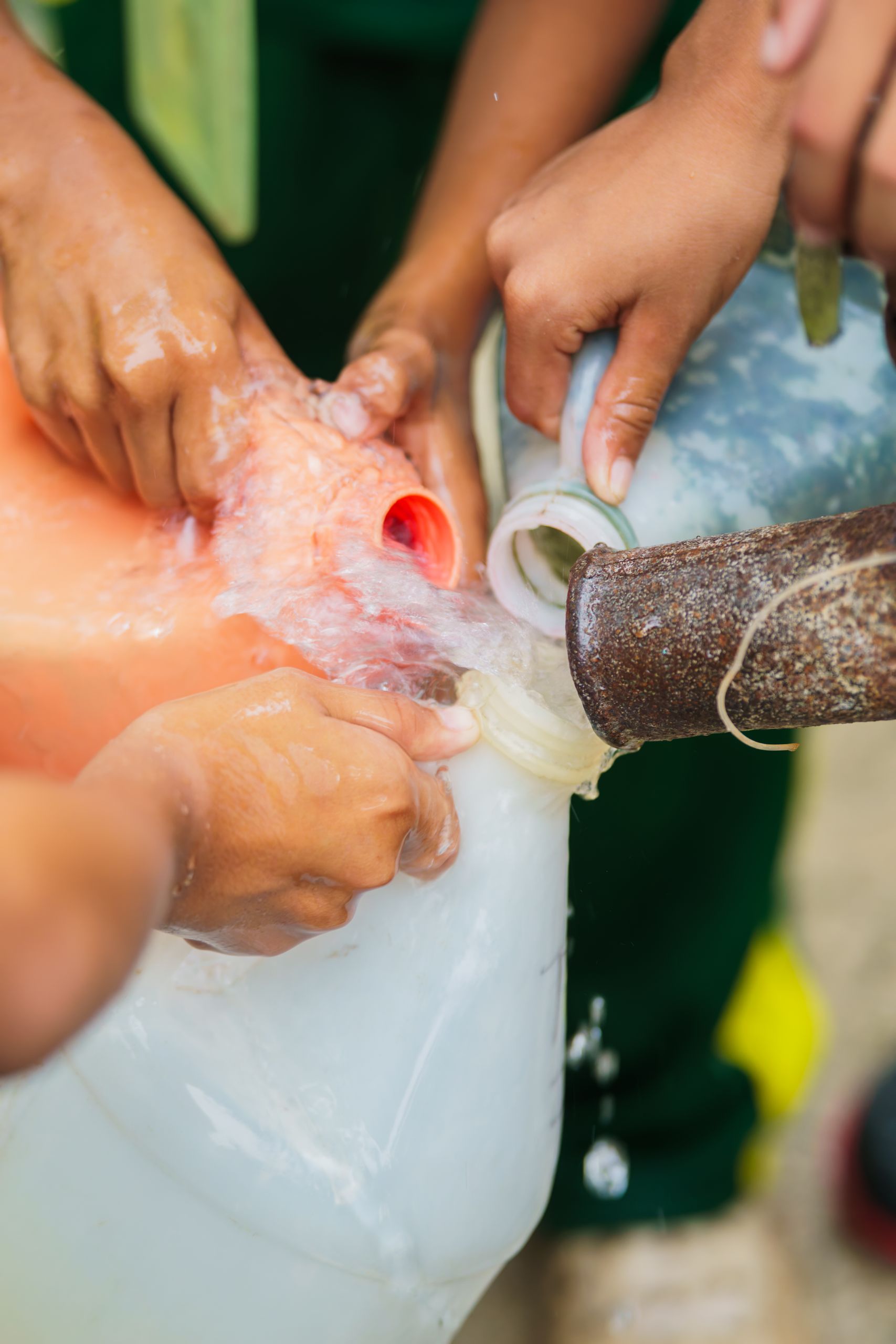 Hands working together to collect water from a communal tap into large jugs.